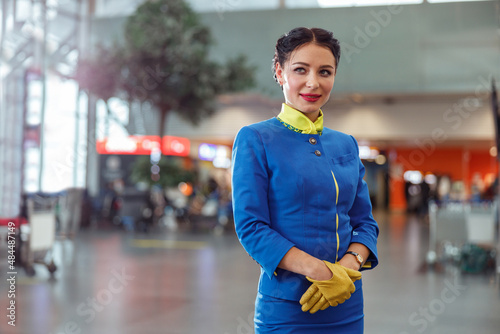 Female flight attendant wearing blue aviation uniform and gloves while looking away and smiling on blurred background
