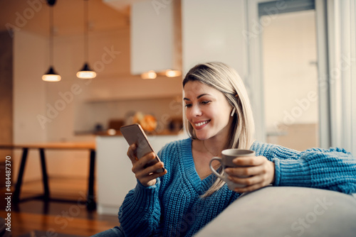 Slika na platnu A happy woman hanging on social media on the phone and drinking coffee at home