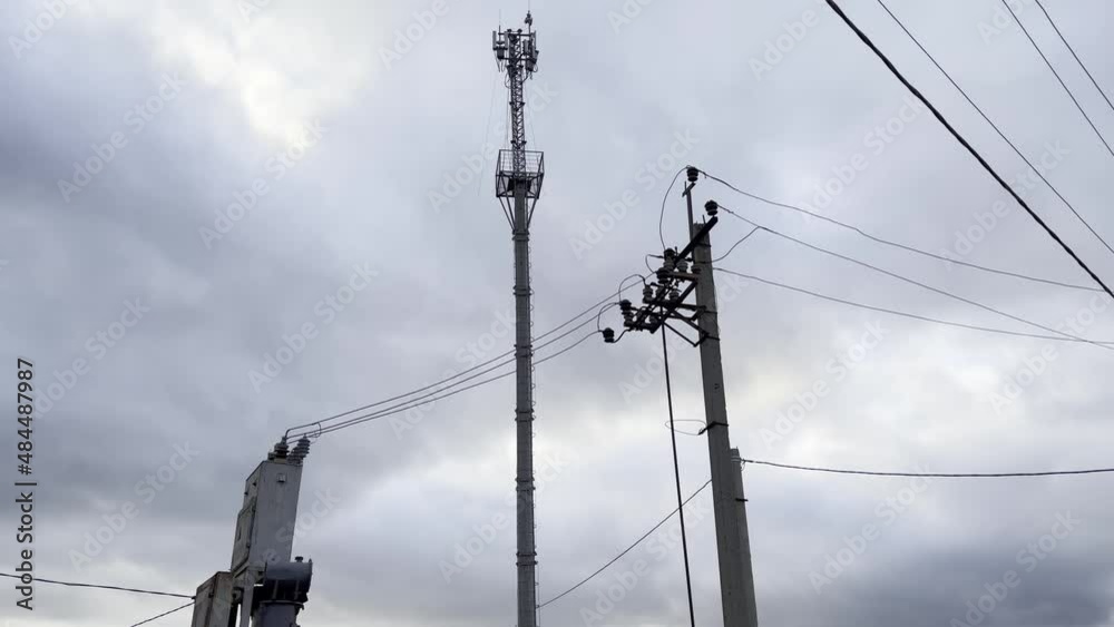 The electric transformer is connected to the power supply system. And a tower with cellular repeaters. Against a cloudy sky.