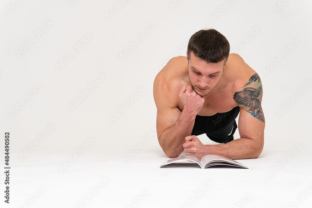 Obraz premium Bodybuilder reads the book on a white background isolated at the bottom of his head on his hands bodybuilder reading, muscle glasses chest muscles, sexy fit. Health winner gym, vision tan