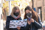 Dos personas (mujeres) turistas orientándose con un mapa y un teléfono en medio de una ciudad.