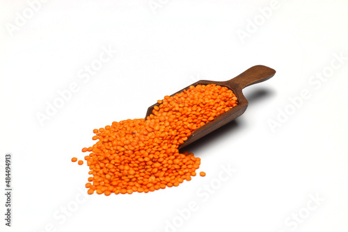 Red lentils in wooden scoop, isolated on white background.