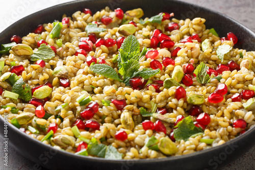 Boiled freekeh with pomegranate, nuts and herbs close-up in a plate on the table. horizontal photo
