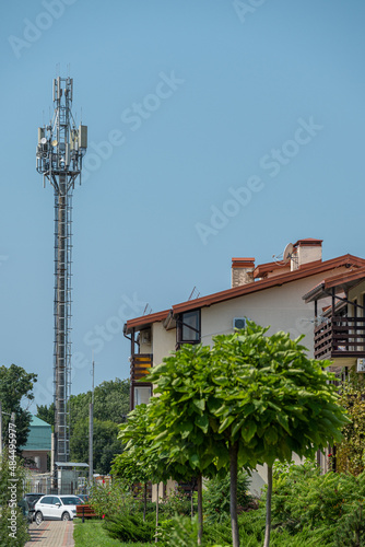 Cellular telecommunications tower with antennas against blue sky stands next to people's homes. Concept of safe global communication of technologies 4G, 5G for people and nature.