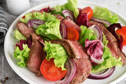 Salad with beef, lettuce and tomatoes on a concrete background.
