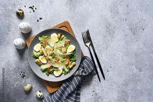 Caesar salad with chicken, sauce, and parmesan on concrete background.