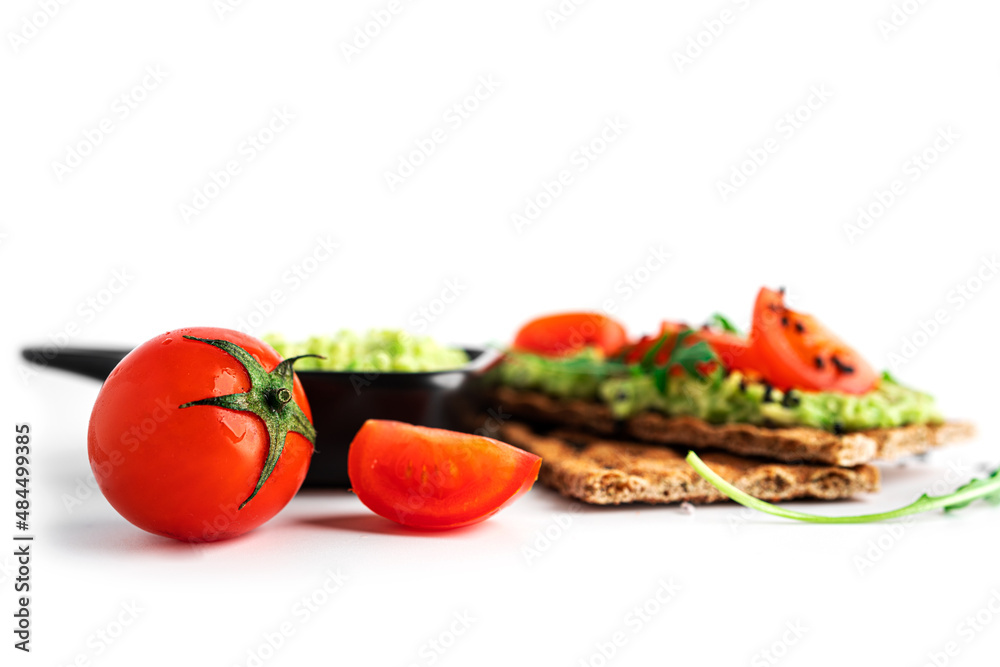 Avocado sandwich with avocado cream and rye crisp bread for snack. Fiber, fitness and diet food. Rye bread with guacamole, arugula and cherry tomatoes isolated on a white background.