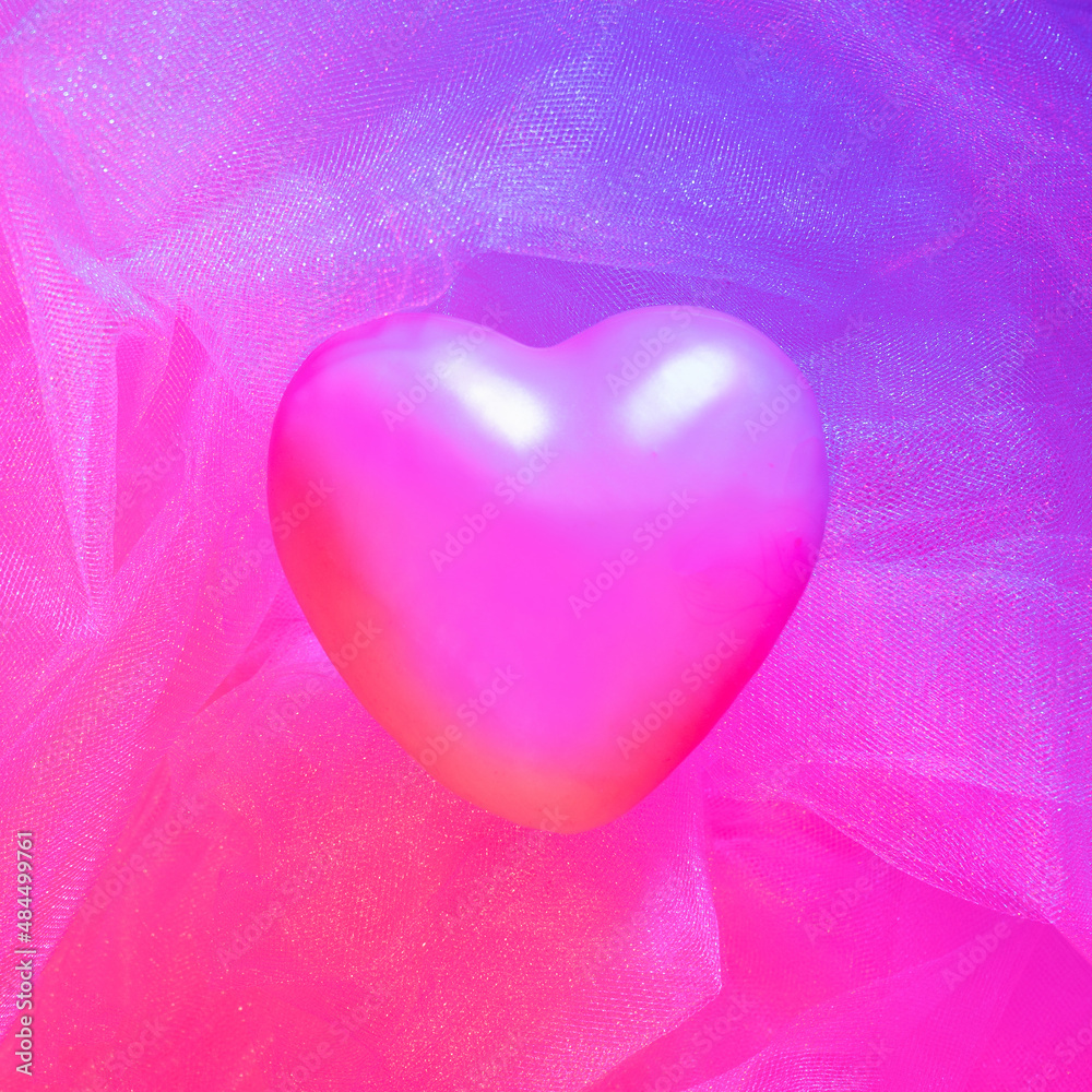 Soft pink heart on light pink tulle fabric enlightened with two colors – blue and red lights. Background from pink crumpled tulle. Background from pink crumpled tulle.