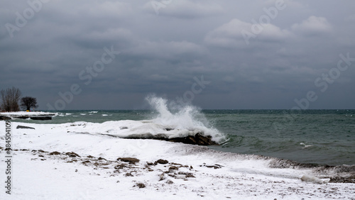 Waves crash dramtically in to an ice berm on the shore of Lake Ontario in winter.