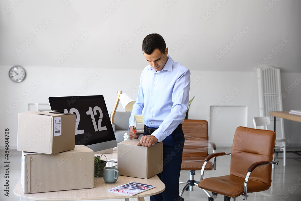 Young man taping box in office on moving day Young man taping box in office on moving day