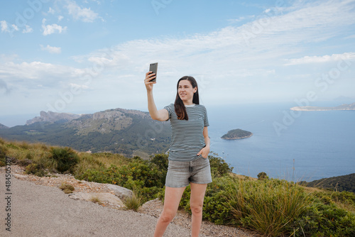 Woman in shorts takes a selfie on the mountain with panoramic view in Italy, Spain or Greece. Summer vacation by the sea. Take pictures on vacation. 