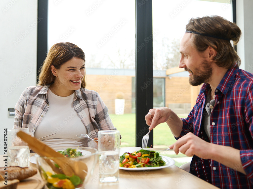 Beautiful loving young Caucasian couple sits at a table and chats cheerfully over a family dinner in a villa overlooking the garden Beautiful loving young Caucasian couple sits at a table and chats cheerfully over a family dinner in a villa overlooking the garden
