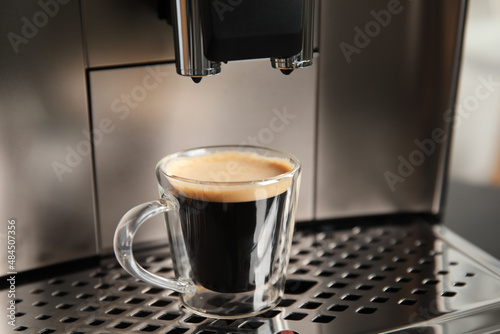 Espresso machine with cup of fresh coffee on drip tray, closeup