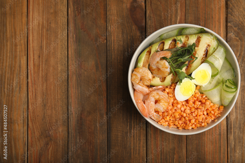 Delicious lentil bowl with avocado, shrimps, egg and cucumber on wooden table, top view. Space for text Delicious lentil bowl with avocado, shrimps, egg and cucumber on wooden table, top view. Space for text