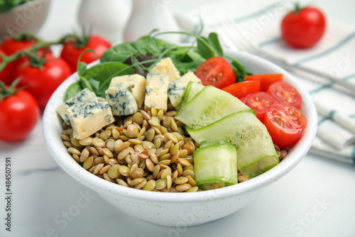 Delicious lentil bowl with blue cheese, tomatoes and cucumber on white marble table