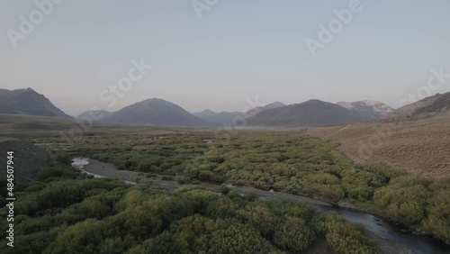 Drone shot over a green field surrounded by mountains