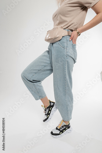 Fashionable woman model in stylish clothes with a handbag and blue jeans in sports sneakers in the studio. Pretty women's feet in fashionable running shoes