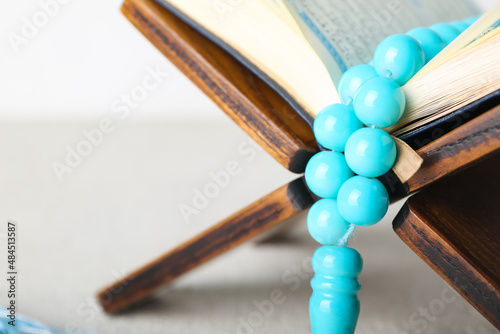 Rehal with Koran and Muslim prayer beads on light background, closeup