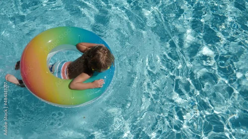 Happy kid playing with colorful swim ring in swimming pool on summer day. Children playing in the swimming pool. Summer activity.