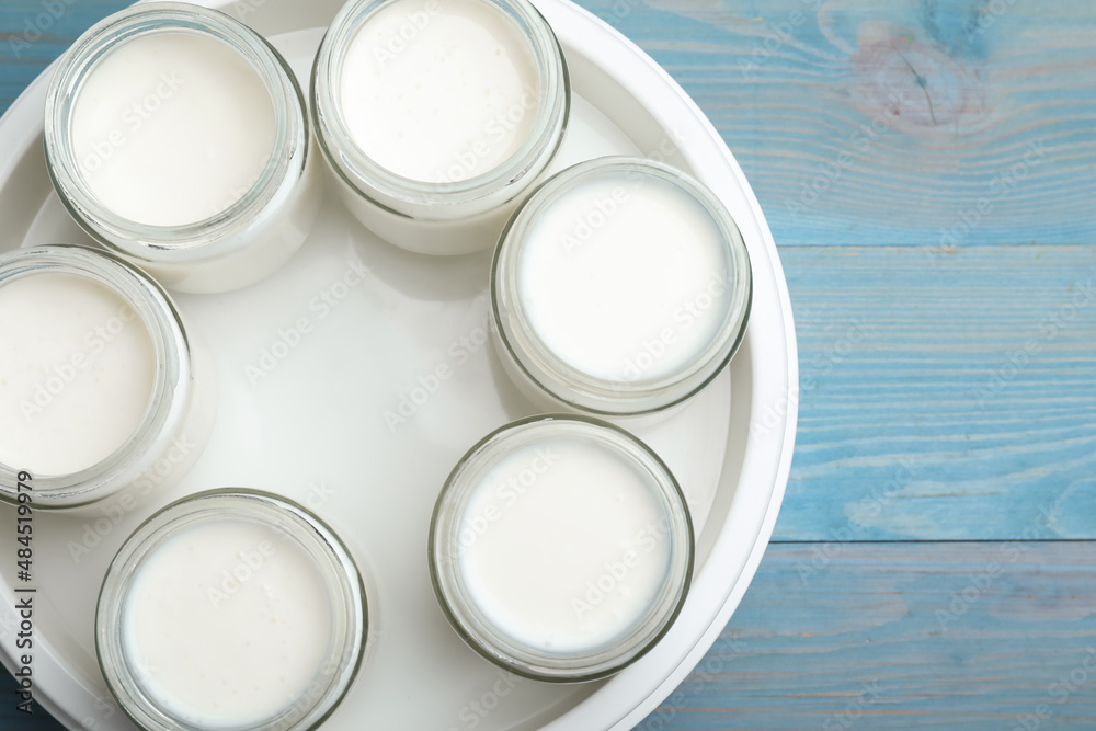 Modern yogurt maker with full jars on blue wooden table, flat lay