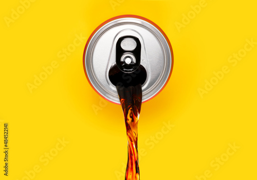 Cola soda can pouring out. Spilling energy or soft drink out of can on isolated yellow background. Concept for unhealthy soda with too much sugar.