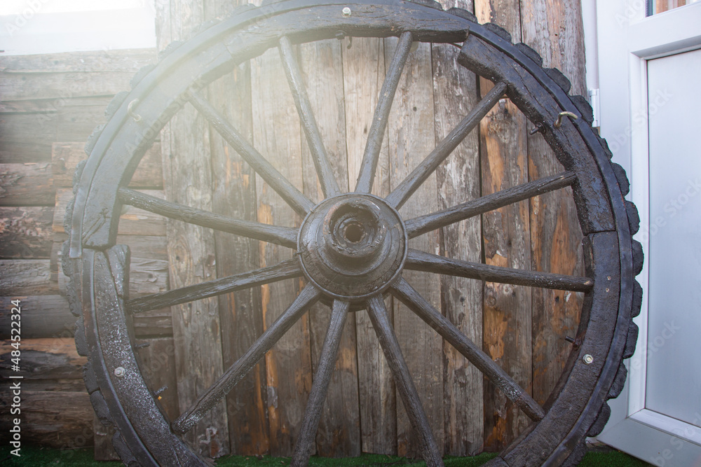 Forgotten old Wooden Wagon Wheel Leaning Against a wooden Wall. Cartwheels at the old wood wall of the house.