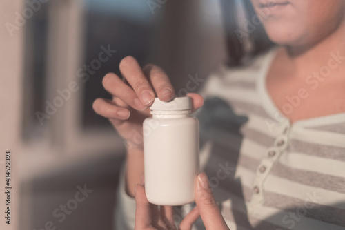 A woman from a white, plastic bottle takes the necessary vitamins for a healthy life