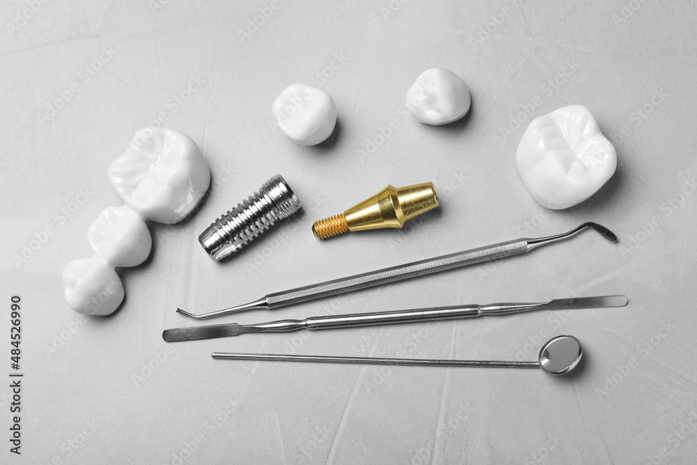 Post, abutment and different crowns of dental implant near medical tools on grey table, flat lay Post, abutment and different crowns of dental implant near medical tools on grey table, flat lay