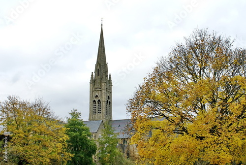 Church with a steeple, surrounded by autumn foliage, on the bank of the River Avon in Bath, England