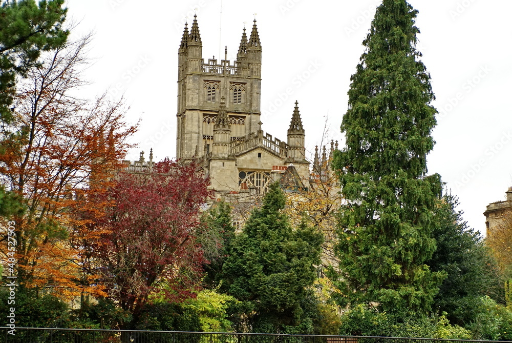 Obraz premium Bath Abbey surrounded by autumn foliage in Bath, England, seen from the bank of the River Avon