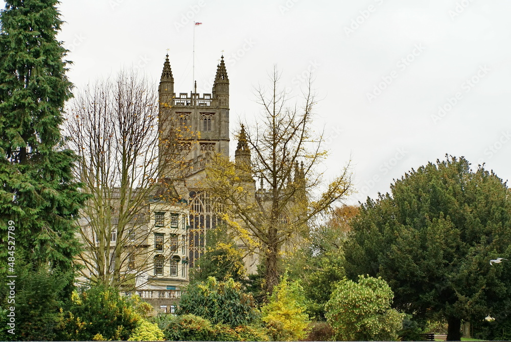 Bath Abbey surrounded by autumn foliage in Bath, England, seen from the bank of the River Avon