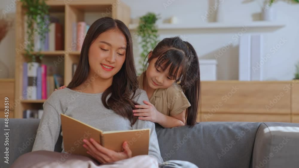 Lovely beautiful Asian single mom reading a book or fairy tale to preschool little cute daughter on the sofa at home. Parenting and teaching activities. Bonding enjoying family lifestyle hobby at home Lovely beautiful Asian single mom reading a book or fairy tale to preschool little cute daughter on the sofa at home. Parenting and teaching activities. Bonding enjoying family lifestyle hobby at home