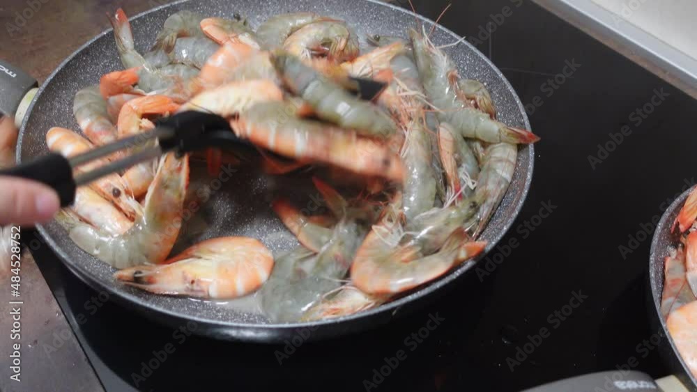 Cook fries raw fresh king prawns for dinner stirring with plastic spatula on pan at modern stove IN kitchen at home close view Cook fries raw fresh king prawns for dinner stirring with plastic spatula on pan at modern stove IN kitchen at home close view