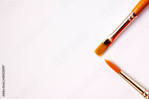 Flat lay of artistic orange metal wooden paint brushes close up on white background with copy space from above. Drawing and design concept work tools on the right
