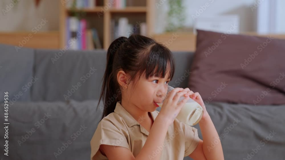 Slow motion - Portrait of cute asian little girl drinking milk sits at the living room. Child with a glass of milk before breakfast. children healthy concept.
