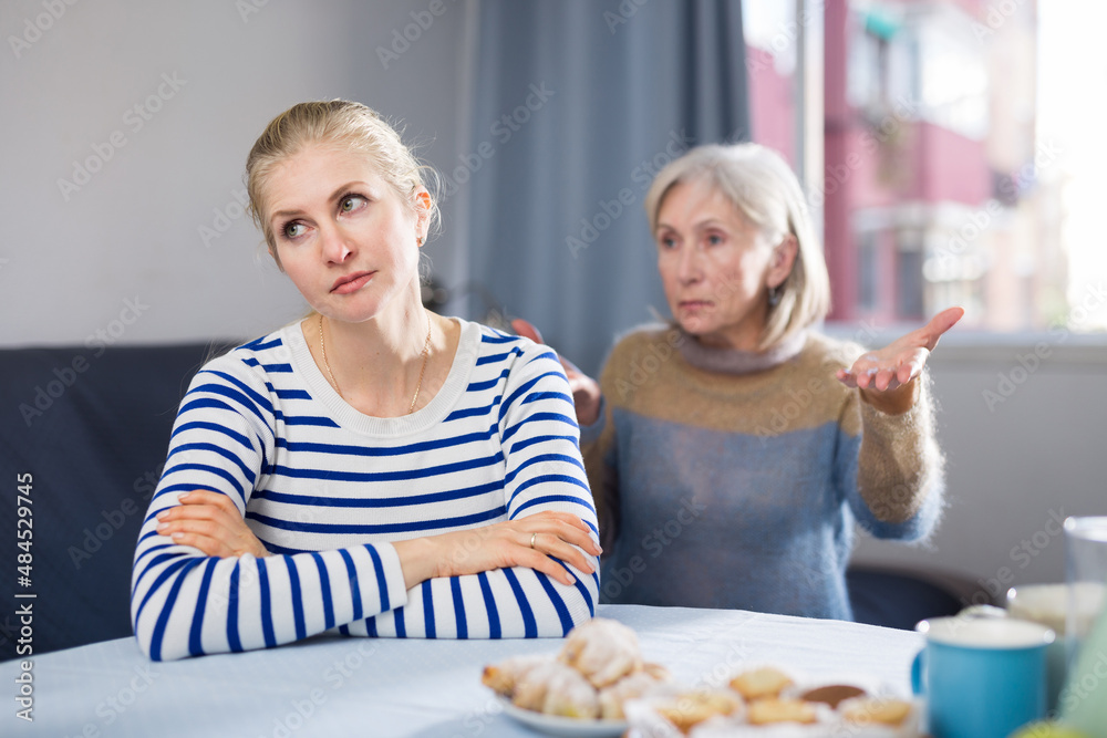 Mature woman scolds her adult daughter, sitting at the table