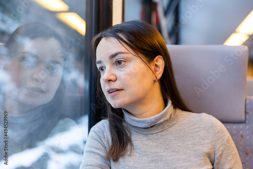 Dark-haired female traveler enjoying journey in modern comfortable train, looking with interest at picturesque scenery outside window photo