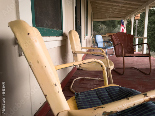 Vintage, metal armchairs on outdoor covered porch of cabin. Faded yellow and burgundy chairs with paint chipping off