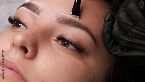 Master applies white markings to correct shape of eyebrows with a special brush. The beautiful face of young girl model on sofa in a beauty salon before microblading, permanent makeup eyebrow tattoo
