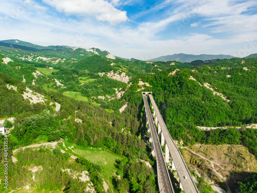 Aerial view of divided highway entering a mountain tunnel among fields and hills surronding San-Marino microstate. Beautiful nature of Emilia-Romagna region of Italy.