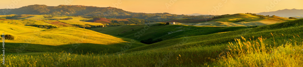 Stunning morning view of fields and farmlands with small villages on the horizon. Summer rural landscape of rolling hills, curved roads and cypresses of Tuscany, Italy.