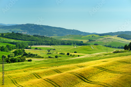 Stunning view of fields and farmlands with small villages on the horizon. Summer rural landscape of rolling hills, curved roads and cypresses of Tuscany, Italy.