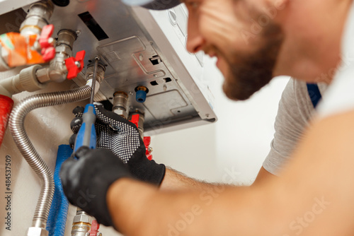 Closeup of plumber using screwdriver while installing new steel hot water central heating system in apartment photo
