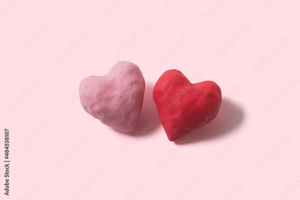 Two love hearts made of plasticine with textures on the pink background