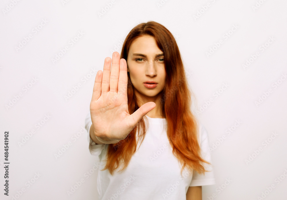 Portrait of a serious young redhair woman standing with outstretched hand showing stop gesture Portrait of a serious young redhair woman standing with outstretched hand showing stop gesture