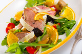 Healthy salad with delicate roasted duck fillet, cheese, fresh greens, tomato cherry, onion, prune and orange slice served on white plate