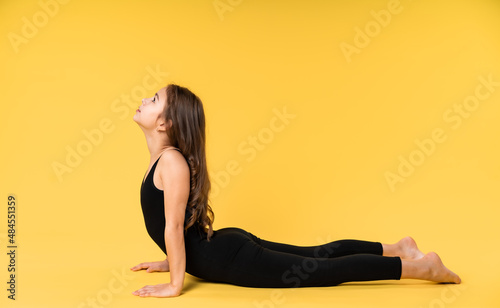 girl gymnast studio. little gymnast trains, shows a gymnastic element. do sport. Isolated on a colored yellow background. Young girl gymnast