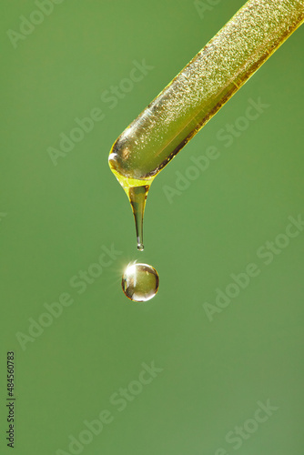 A drop of cosmetic aromatic oil drips from the pipette. Front view.