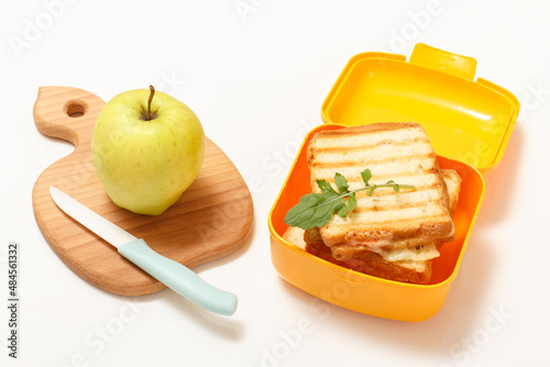 Yellow lunch box with toasted slices of bread, cheese and green parsley.