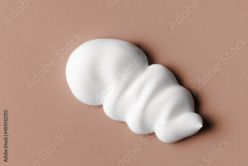 White cream texture. Cosmetic creamy product on brown background. Sunscreen, face creme, body lotion, hair conditioner swirl swatch closeup photo